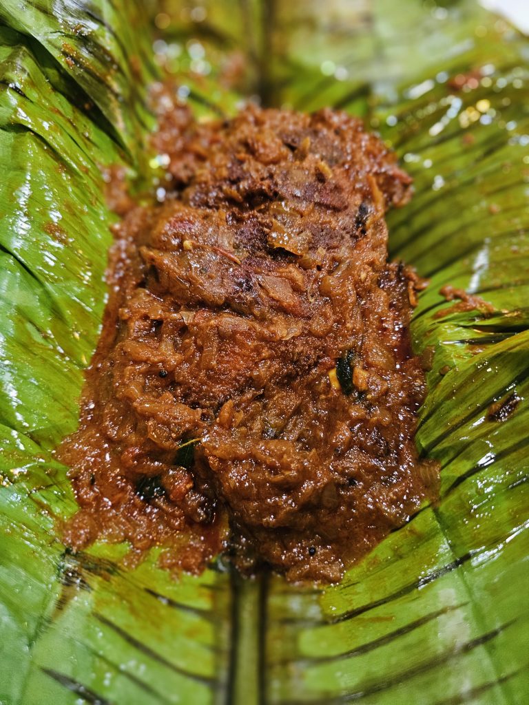 A traditional Kerala-style dish, pearl spot (karimeen) Pollichathu, is served on a fresh green banana leaf, with rich textures, spices, and natural colors that make for an appealing food photograph. Location: Ayamkudy, Kottayam, Kerala.