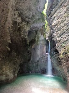 A secluded waterfall cascading down steep rocky cavern cliffs into a clear turquoise natural pool.