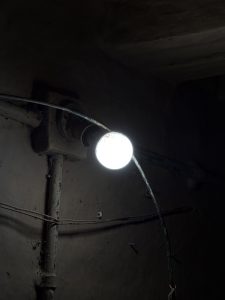 Hanging light bulb illuminating a dark, rough-walled interior with exposed pipes and wires.