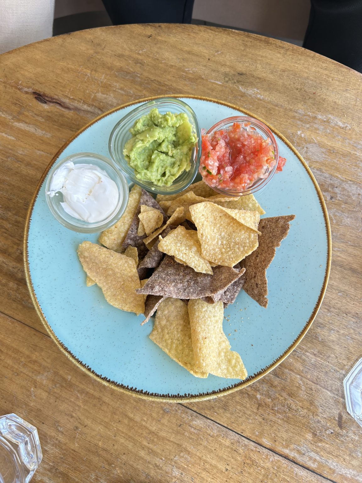 A light blue plate is filled with a mix of tortilla chips, including yellow and dark brown varieties, some of which are slightly curled.