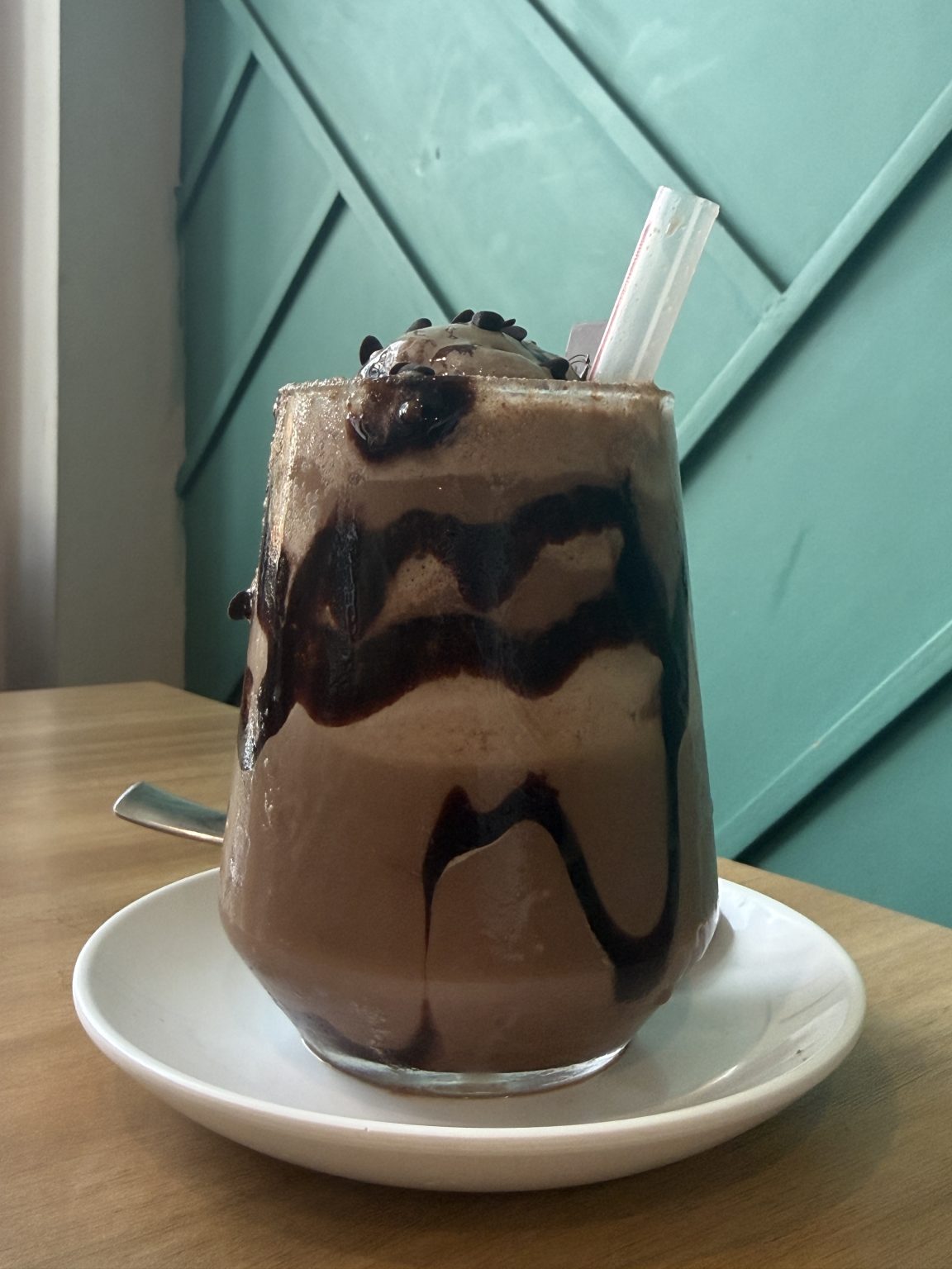 A tall glass filled with a thick, chocolatey drink topped with a scoop of ice cream, drizzled with chocolate syrup.