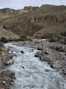 Whitewater river flowing through a rocky mountain canyon with towering cliffs under a cloudy sky.