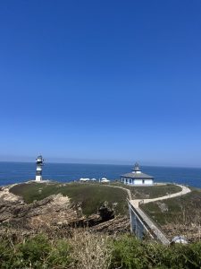 Panoramic view of Isla Pancha Lighthouse on a green islet, surrounded by rocky cliffs and the open sea under a clear blue sky.