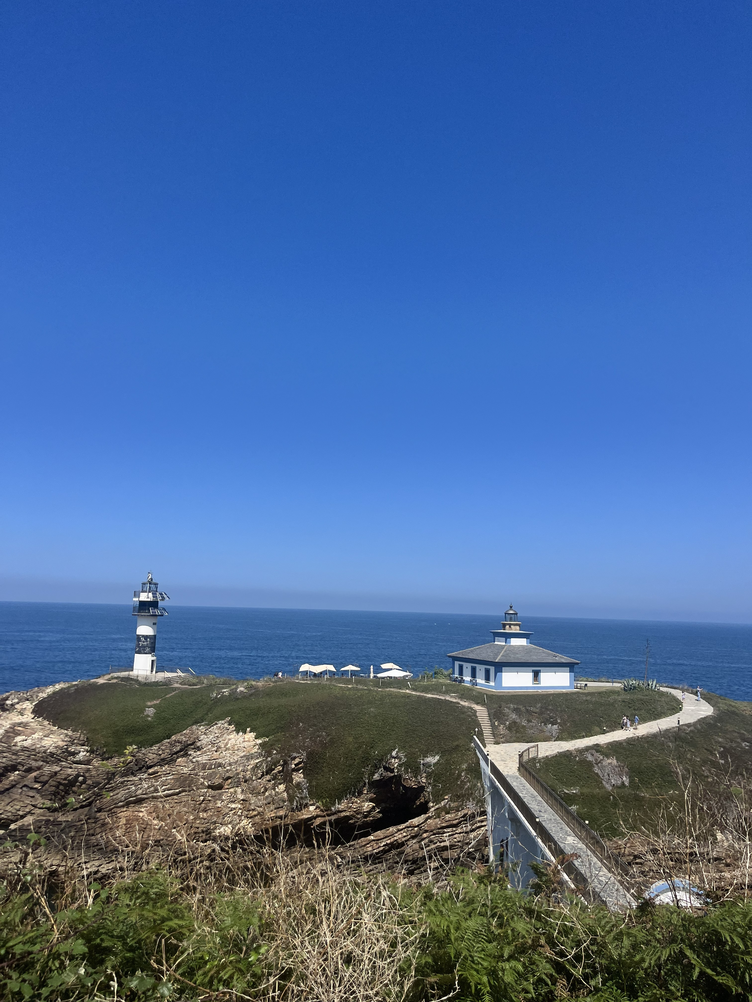 Panoramic view of Isla Pancha Lighthouse on a green islet, surrounded by rocky cliffs and the open sea under a clear blue sky.