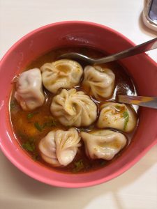 A pink bowl filled with a steaming soup containing six dumplings. 
