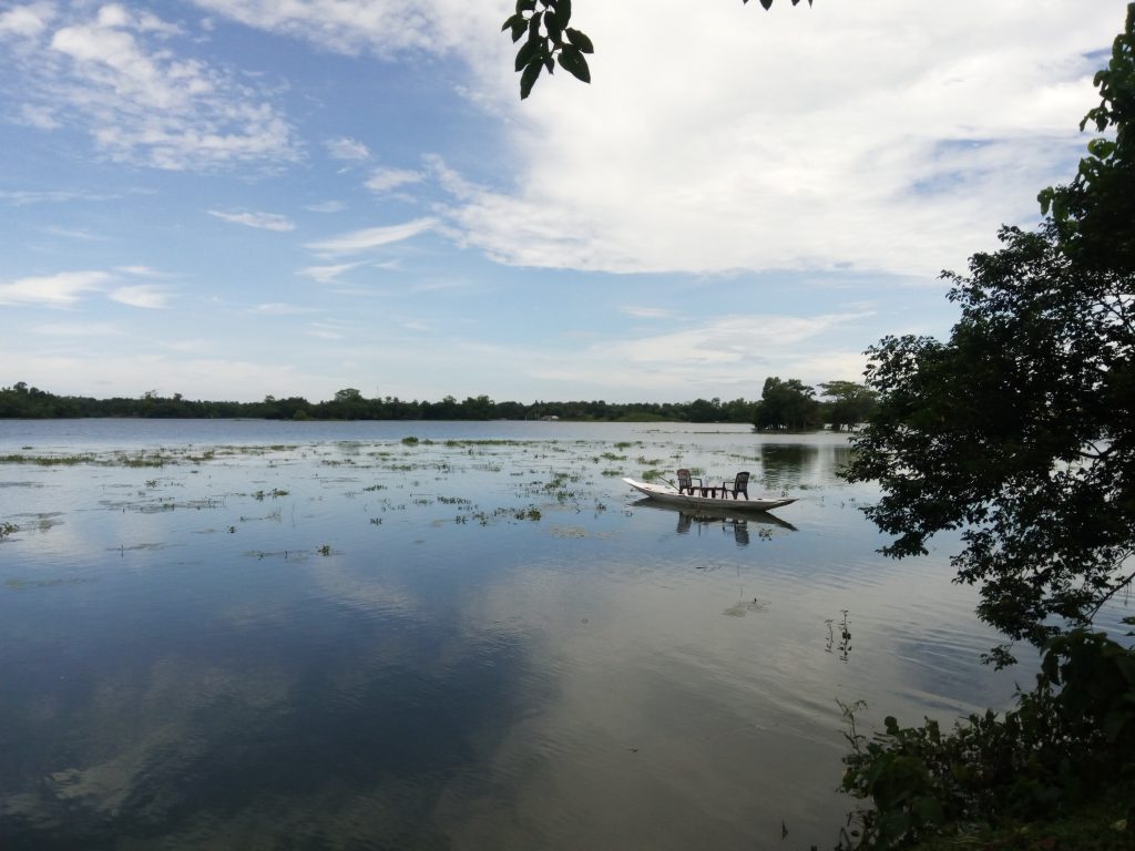A small wooden boat floating on a serene lake under a partly cloudy sky.