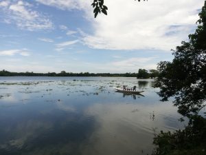 A small wooden boat floating on a serene lake under a partly cloudy sky.