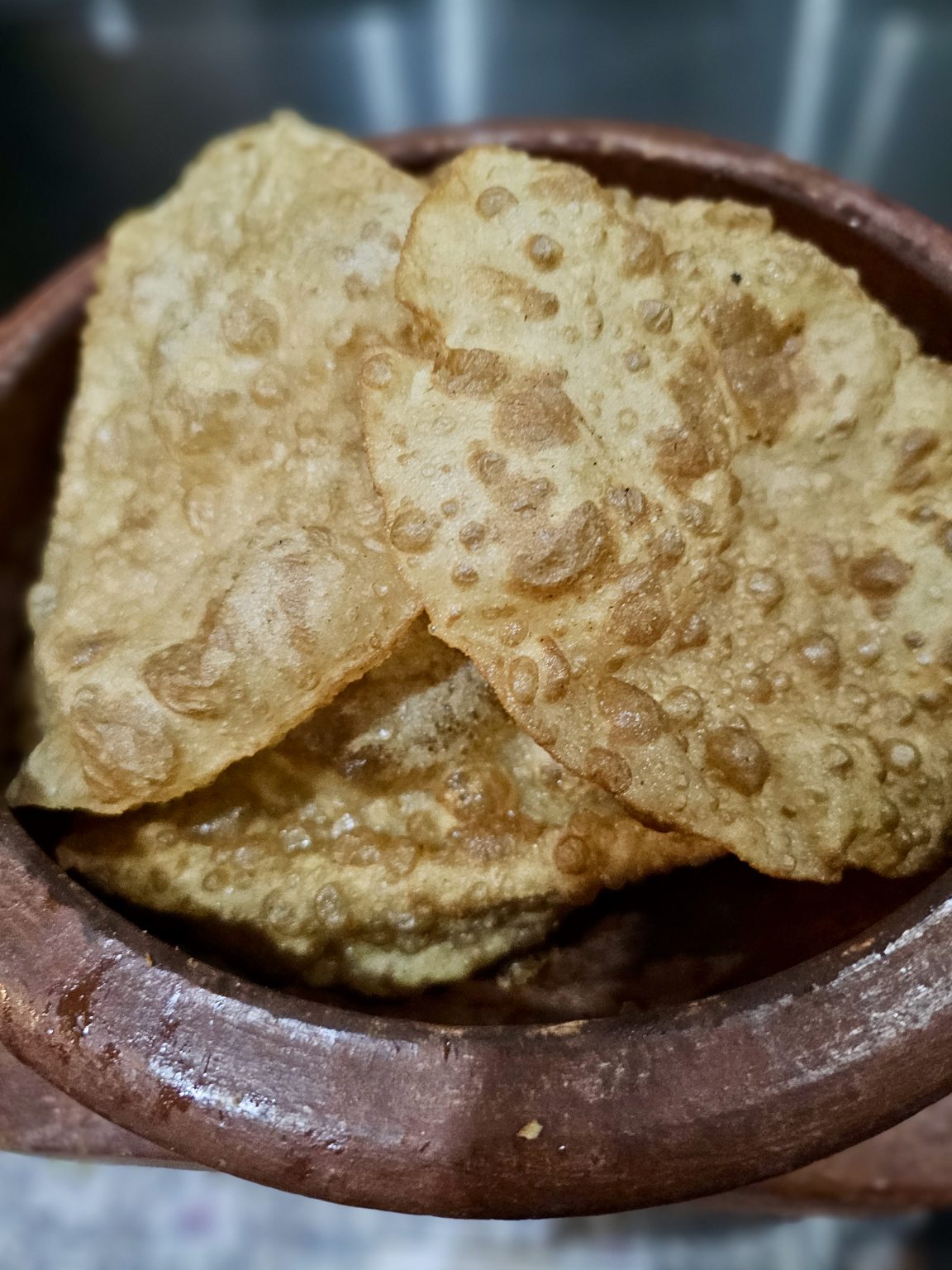 Crispy golden puris stacked in a traditional earthen bowl, with their bubbled texture and toasted surface clearly visible. Location: Ayamkudy, Kottayam, Kerala