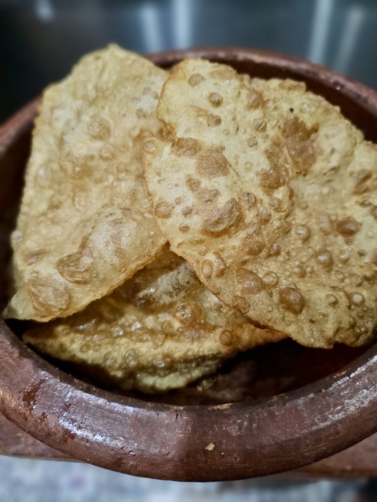 Crispy golden puris stacked in a traditional earthen bowl, with their bubbled texture and toasted surface clearly visible. Location: Ayamkudy, Kottayam, Kerala