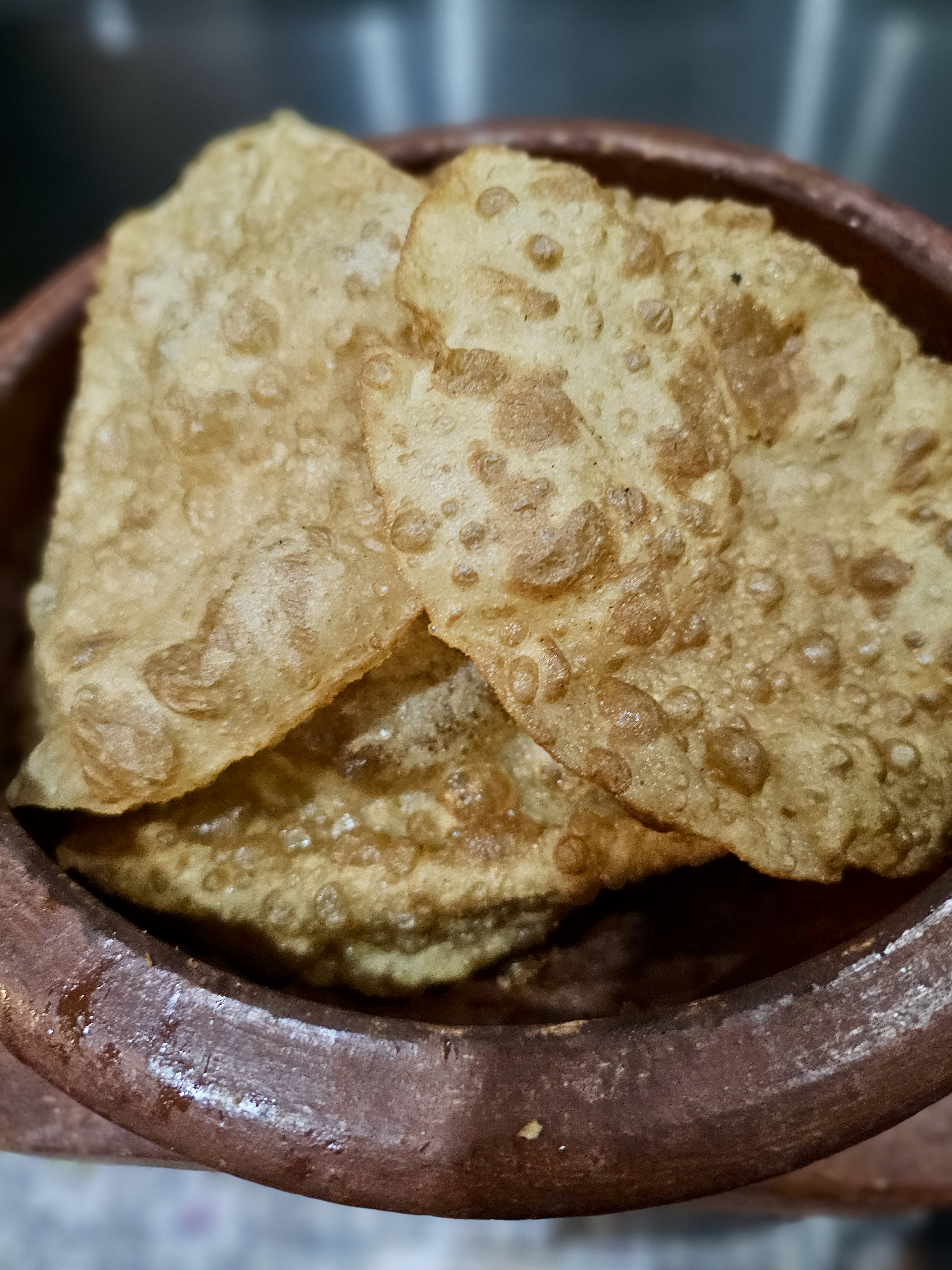 Crispy golden puris stacked in a traditional earthen bowl, with their bubbled texture and toasted surface clearly visible. Location: Ayamkudy, Kottayam, Kerala