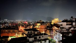 Nighttime rooftop view of Kathmandu city, showing densely packed buildings and glowing city lights with hills in the distance. #WCKTM2026