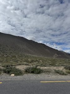 Dry scrubland and a steep mountain slope beyond an asphalt road under a partly cloudy sky.