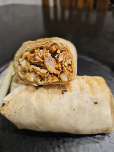 A freshly prepared wrap is shown in close-up, with its cut section revealing a filling of meat, rice, vegetables, and sauce. Warm tones and a shallow depth of field make the food look rich and appetizing. Location: Kuttikkattoor, Kozhikode, Kerala, India.
