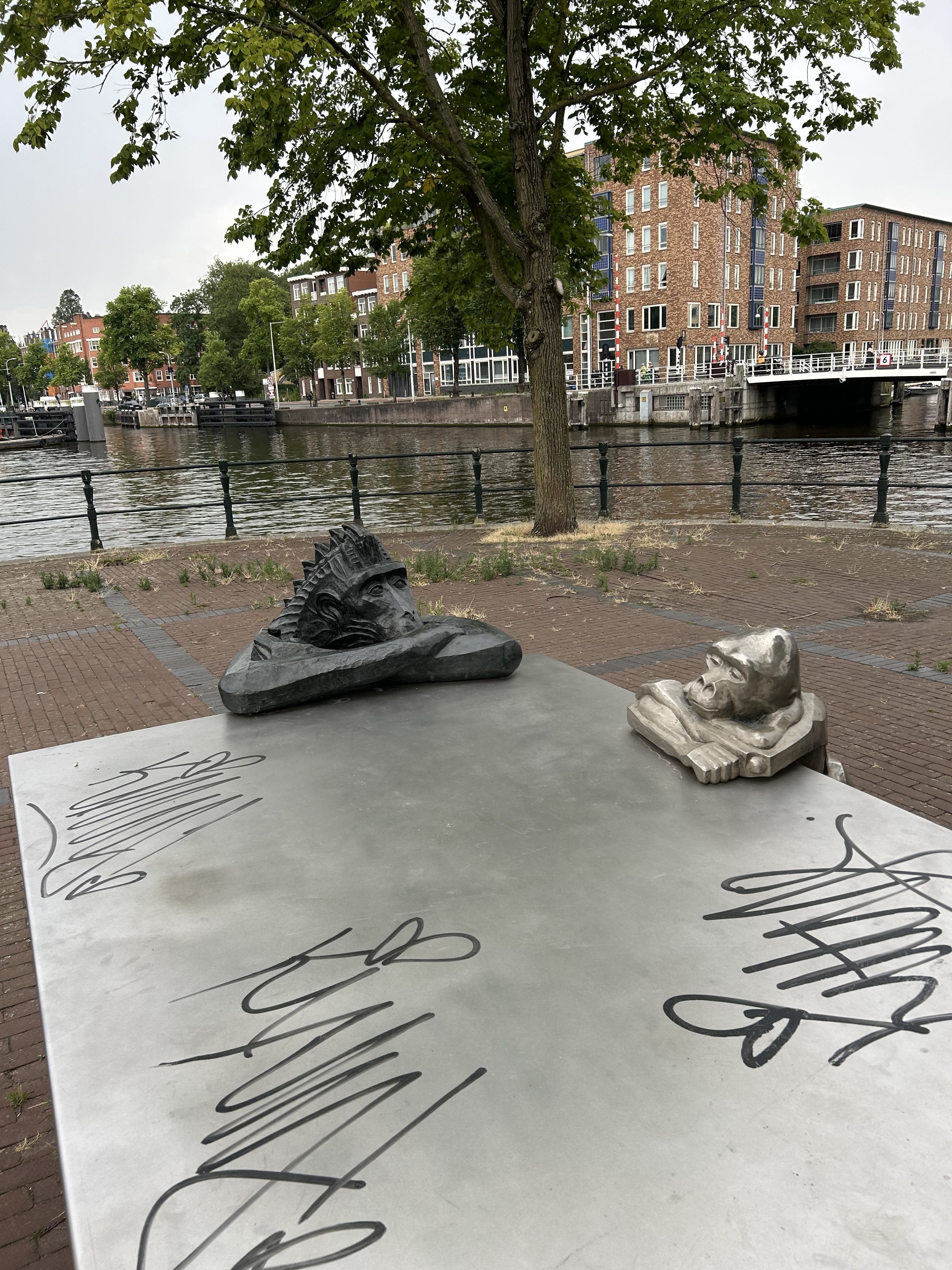Primate sculptures on a metal table with graffiti beside an urban canal.