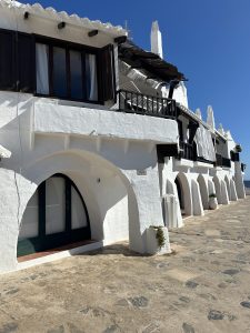 Edificios tradicionales blancos con porches arqueados y balcones de madera junto a una calle empedrada.