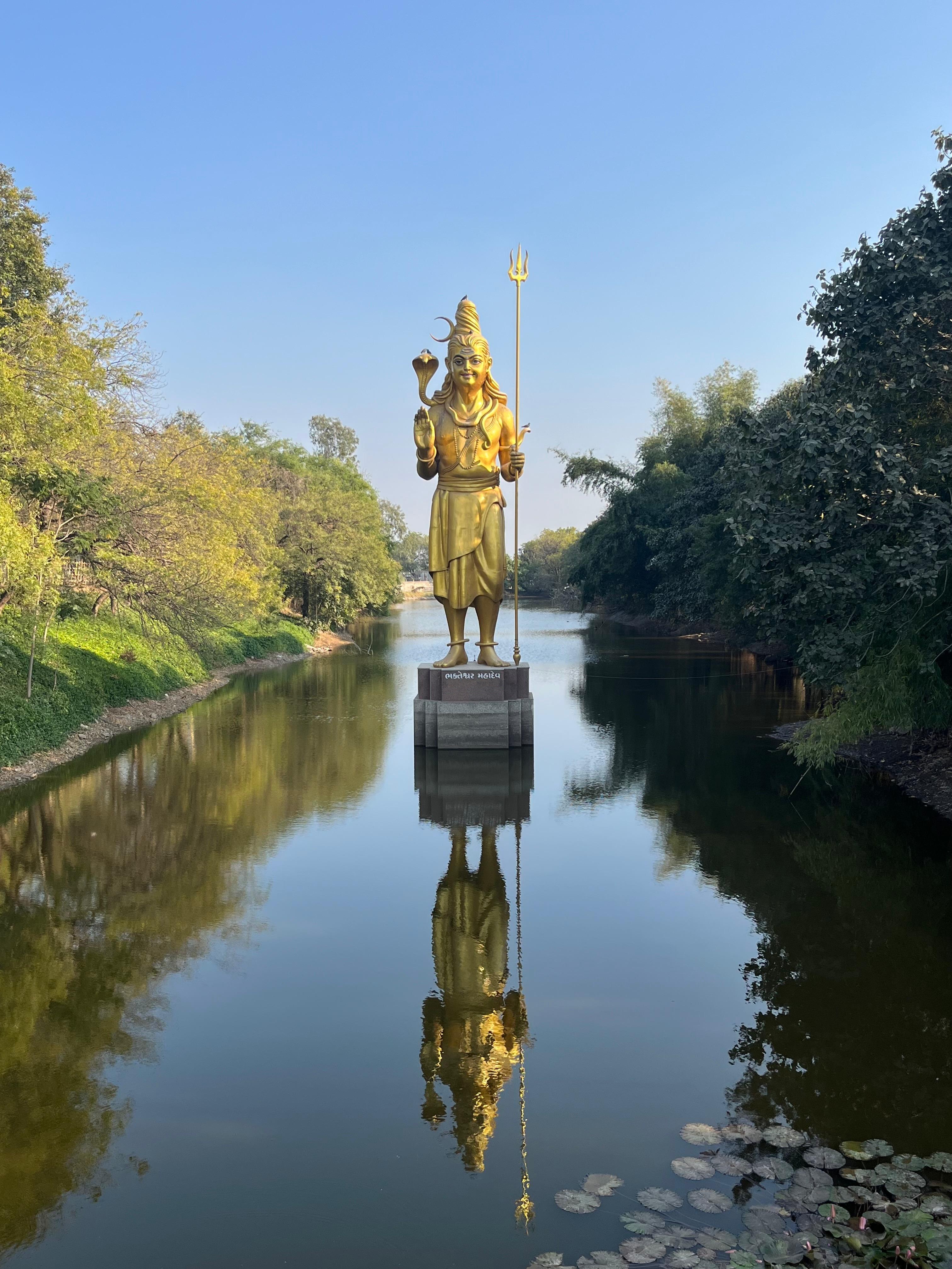 Lord Shiva statue standing beside a river with its reflection in the water