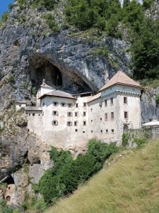 Predjama Castle built directly inside the mouth of a massive cliffside cave surrounded by green forested hills.