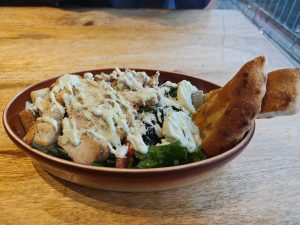 A brown bowl filled with a vibrant salad featuring mixed greens, diced chicken, and cherry tomatoes.
