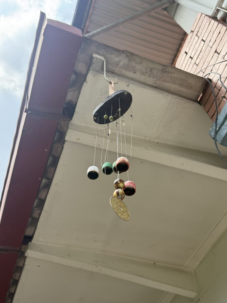 Colorful hanging mobile with patterned spheres and a gold pendant under a sloped roof against a clear blue sky.