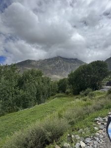 Lush green field with trees and a rocky mountain peak partly covered by clouds.