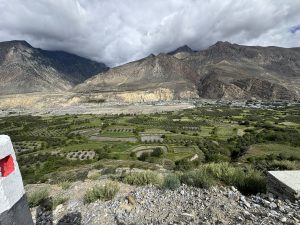 Terraced green farmland and a village in a valley surrounded by dry, rocky mountains under low clouds.