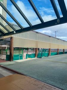 The top of the frame features dark metal framing holding transparent roof panels, allowing natural light to filter down onto the walkway.