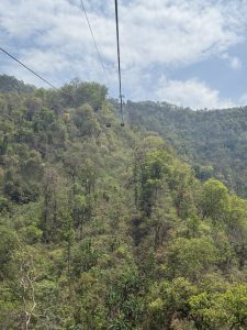 Cable car gondolas traveling over a lush green hillside under a partly cloudy sky.