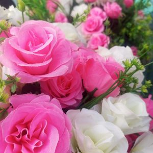 

Close-up of vibrant pink and white artificial roses with layered petals, green leaves, and stems.