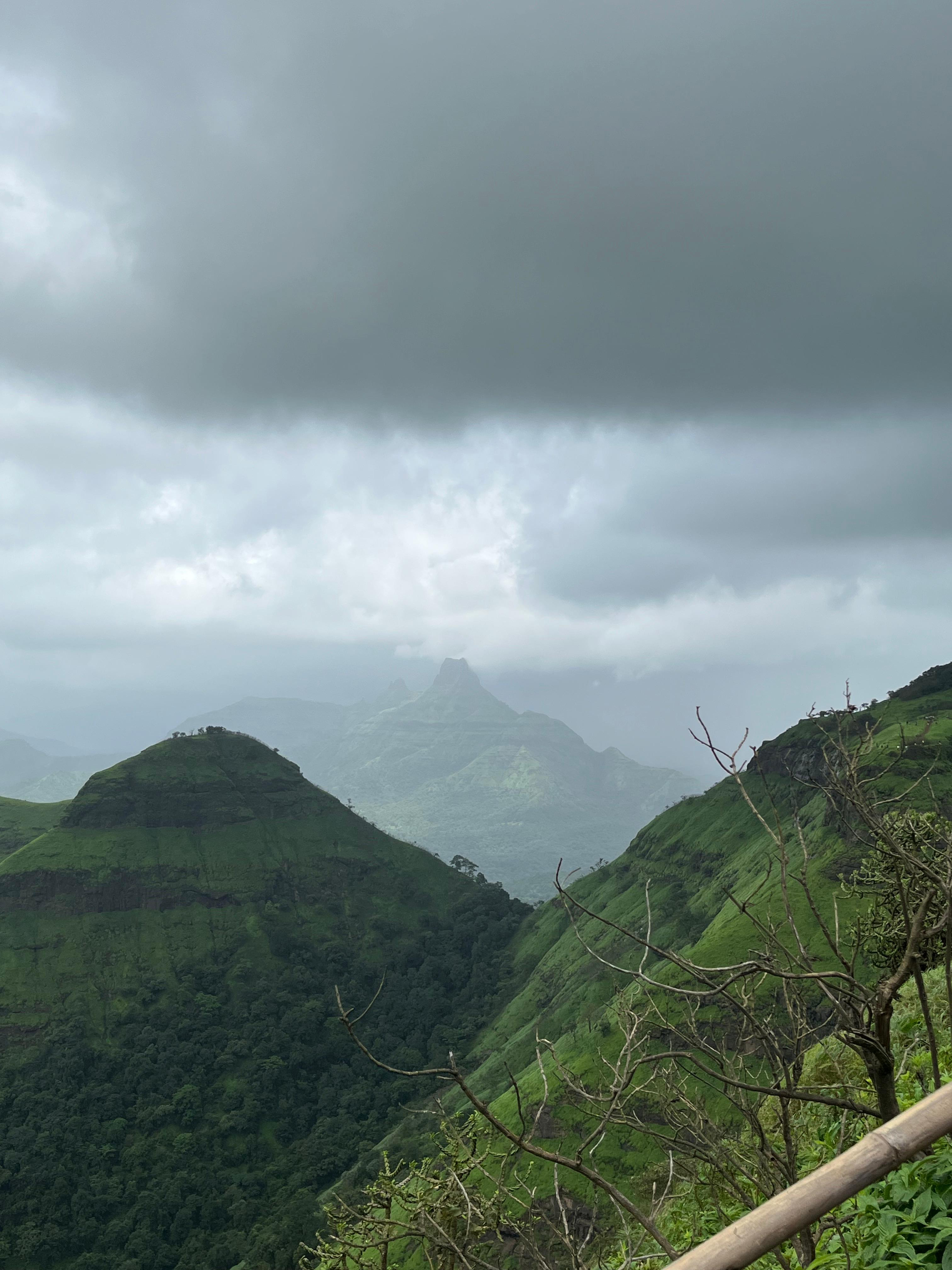 Misty green mountain valley beneath dramatic dark clouds, with a rugged peak rising in the distant landscape.