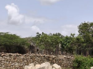 Low stone wall with green trees and a ruined building in the background under a partly cloudy sky.
