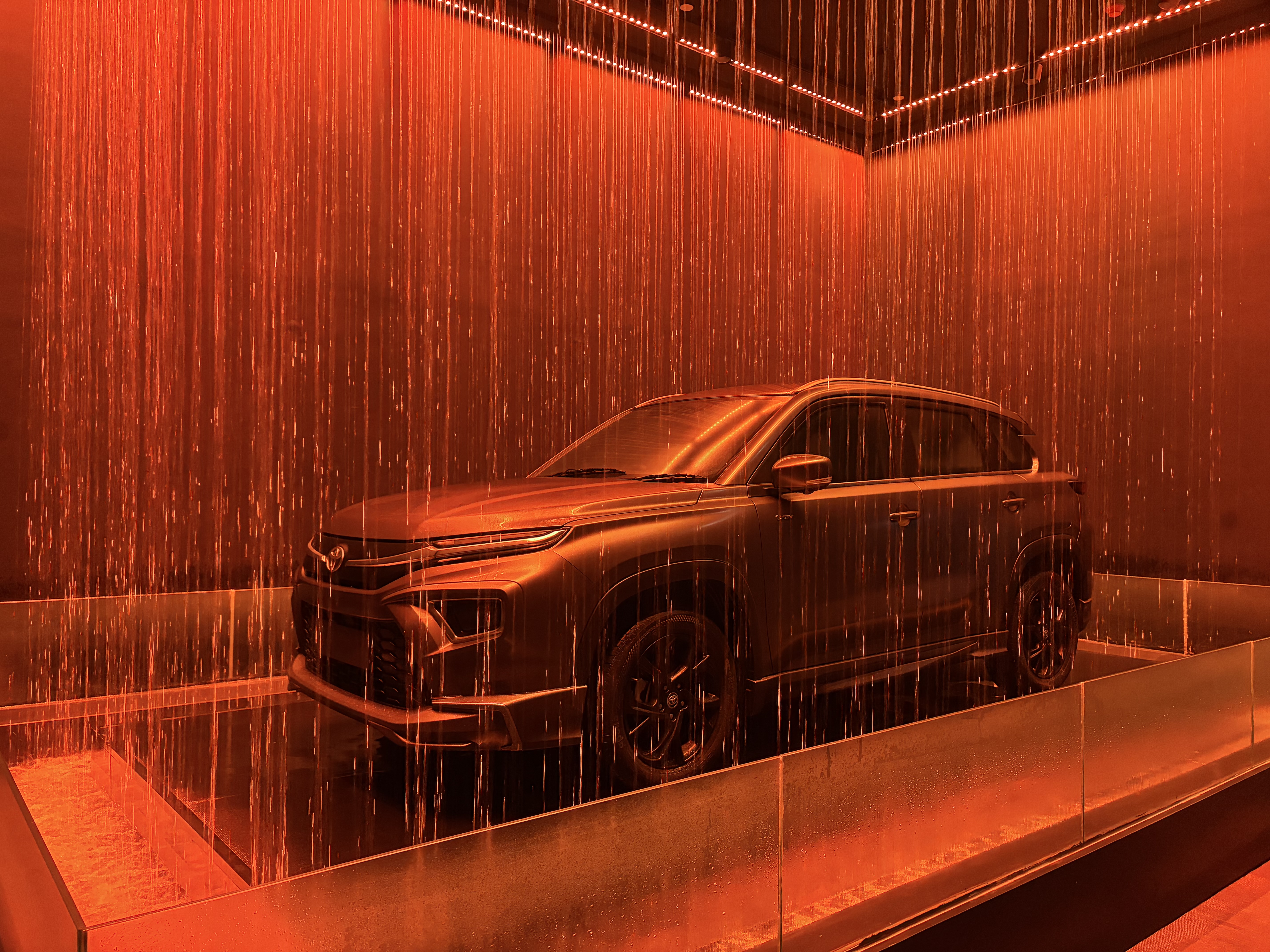 Toyota SUV displayed at a modern exhibition booth behind a curtain of falling water under red lighting.