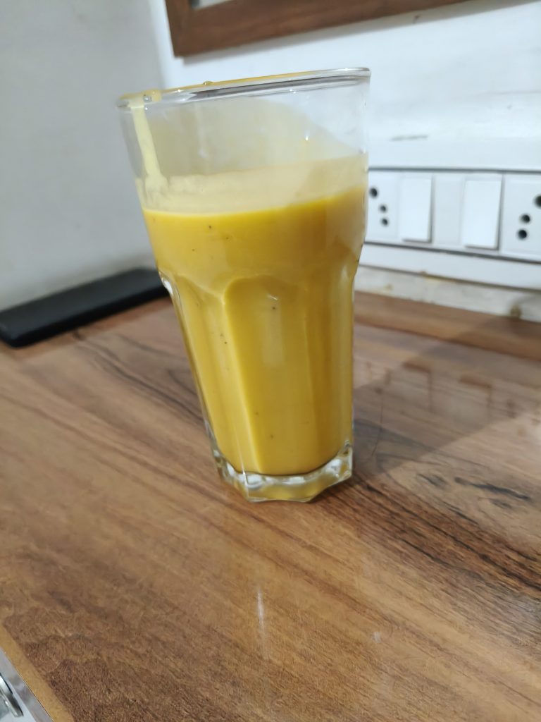 Tall clear glass filled with bright yellow mango juice on a wooden table.
