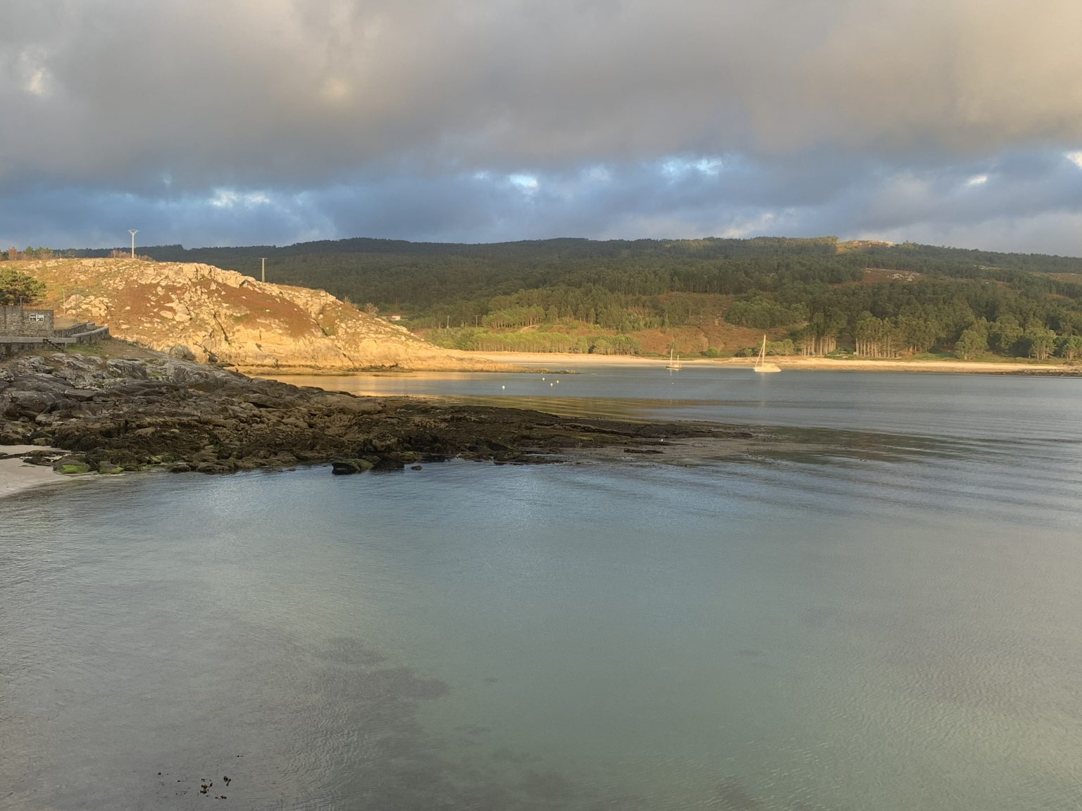 Warm sunlight crossing a sheltered rocky cove beneath dark clouds.