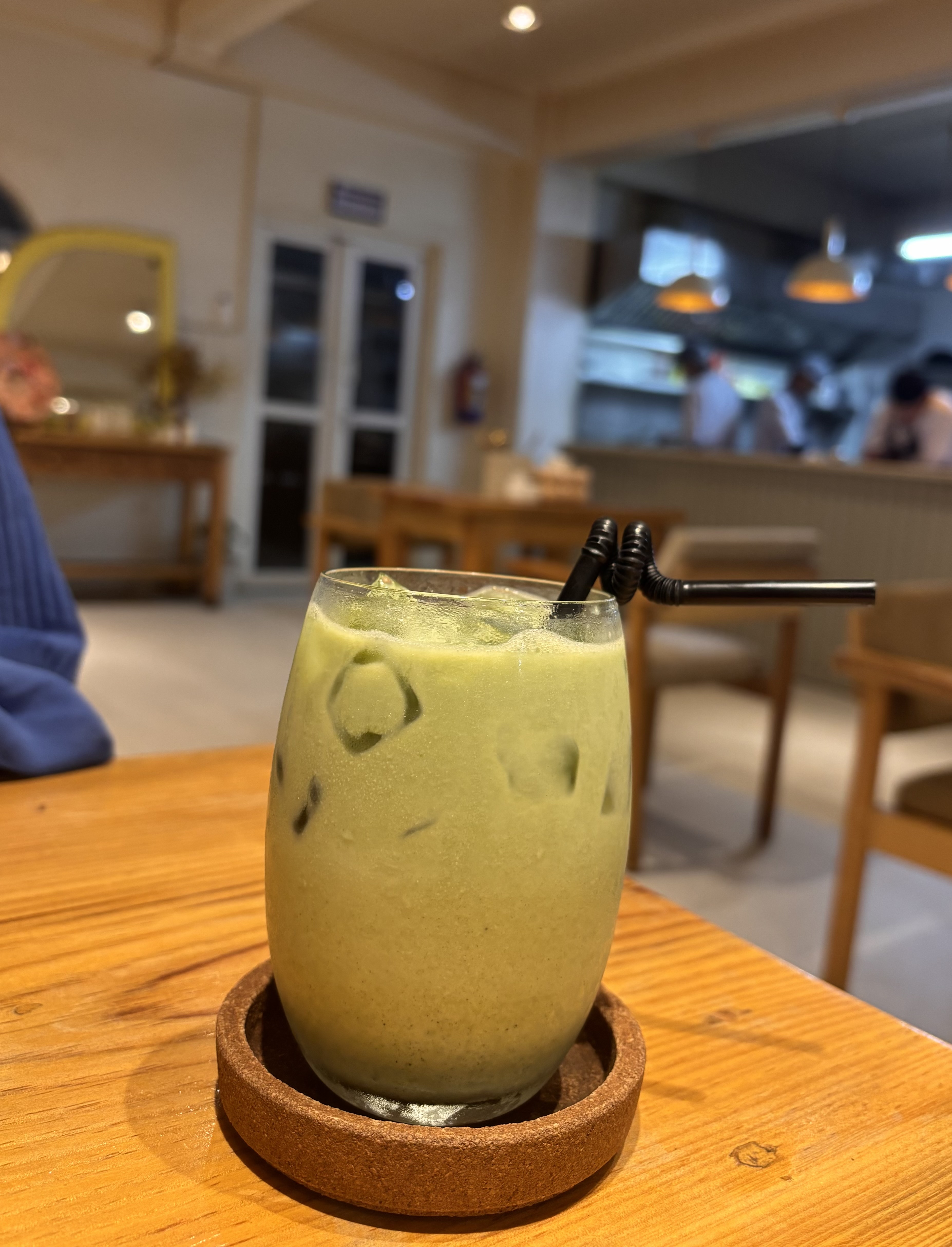 A glass filled with a creamy green drink sits on a wooden table.
