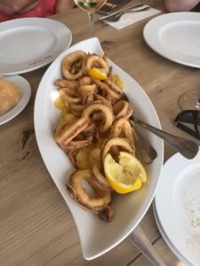 Plate of crispy fried calamari rings on potato chips with two lemon slices.