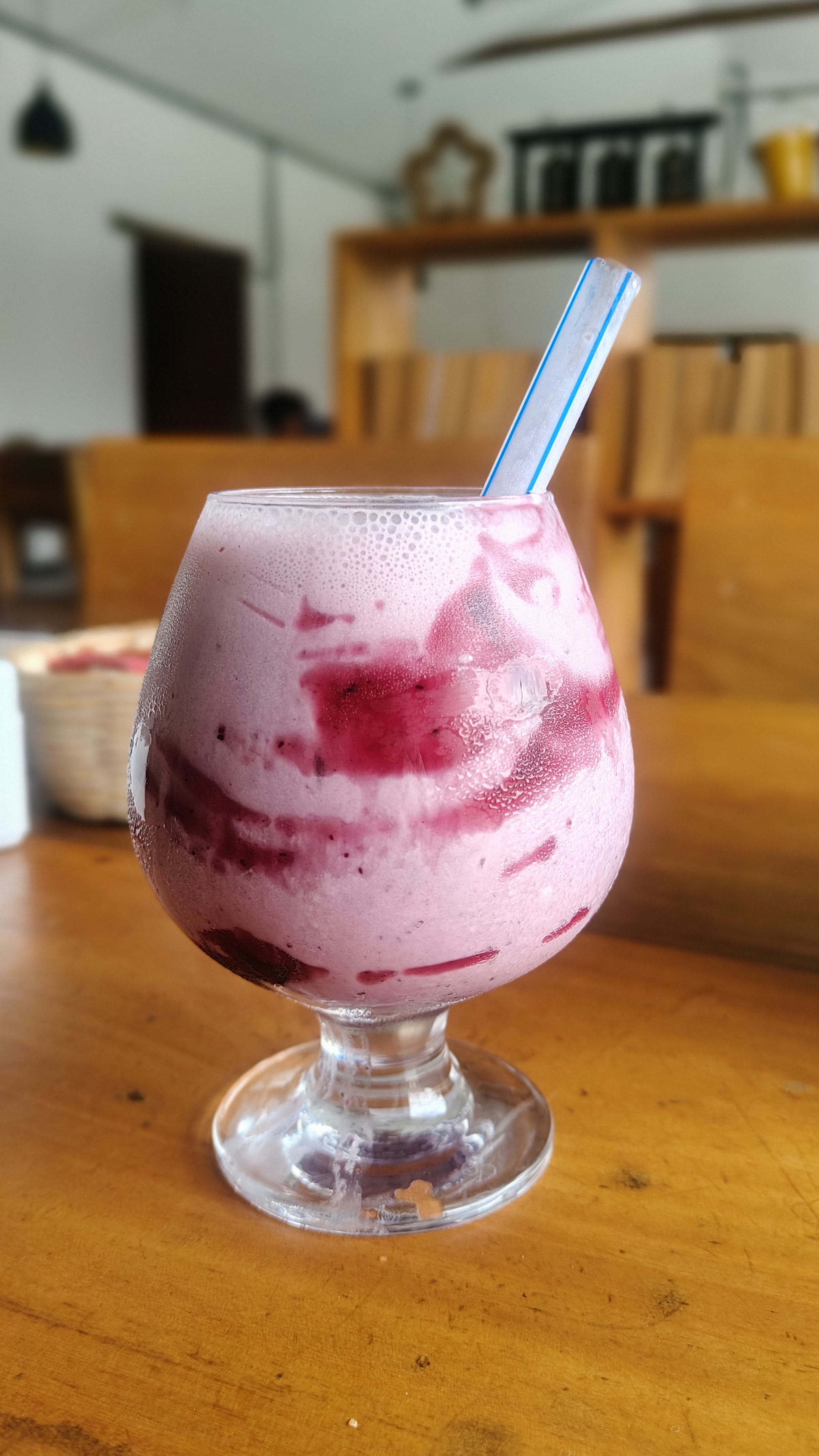 A pink berry smoothie served in a glass with a straw on a wooden table.