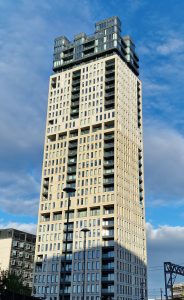 Vertical shot of a tall modern residential building with light stone cladding and glass balconies against a blue sky with soft white clouds.