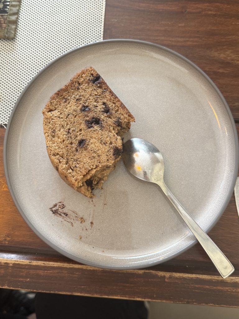 A slice of brown, moist cake sits on a light-colored plate.