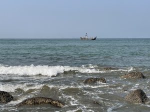 Beautiful ocean view at Cox’s Bazar with rocks in the foreground and a fishing boat in the distance.