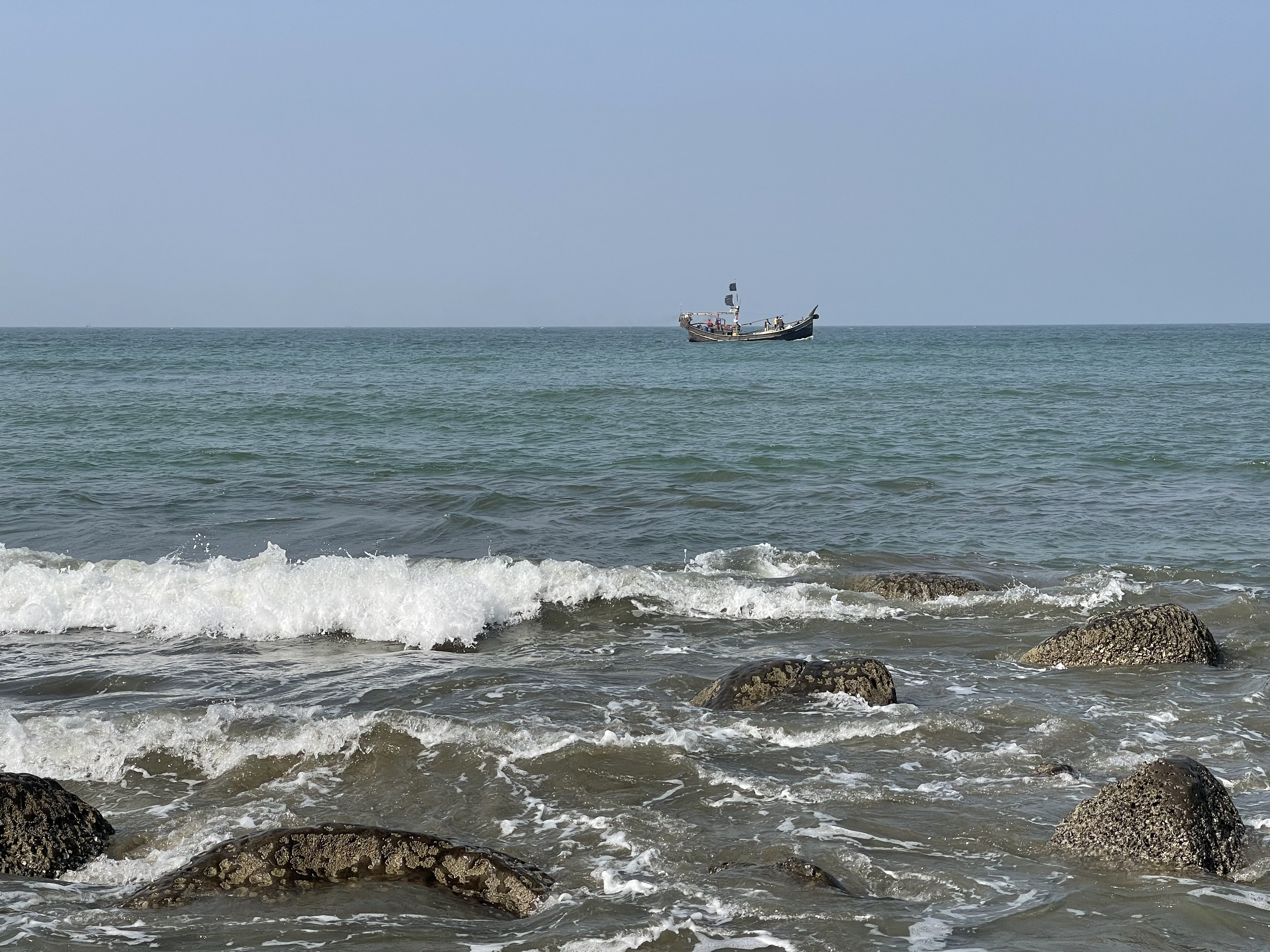 Beautiful ocean view at Cox’s Bazar with rocks in the foreground and a fishing boat in the distance.