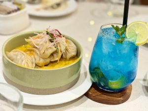 A bowl of dumplings in creamy yellow sauce served alongside a bright blue lime and mint drink. 
