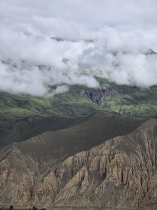 Aerial view of eroded beige mountains and green slopes partly covered by clouds.