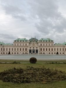 Upper Belvedere Palace in Vienna featuring Baroque white architecture, green roofs, and a large reflecting pond under an overcast sky.