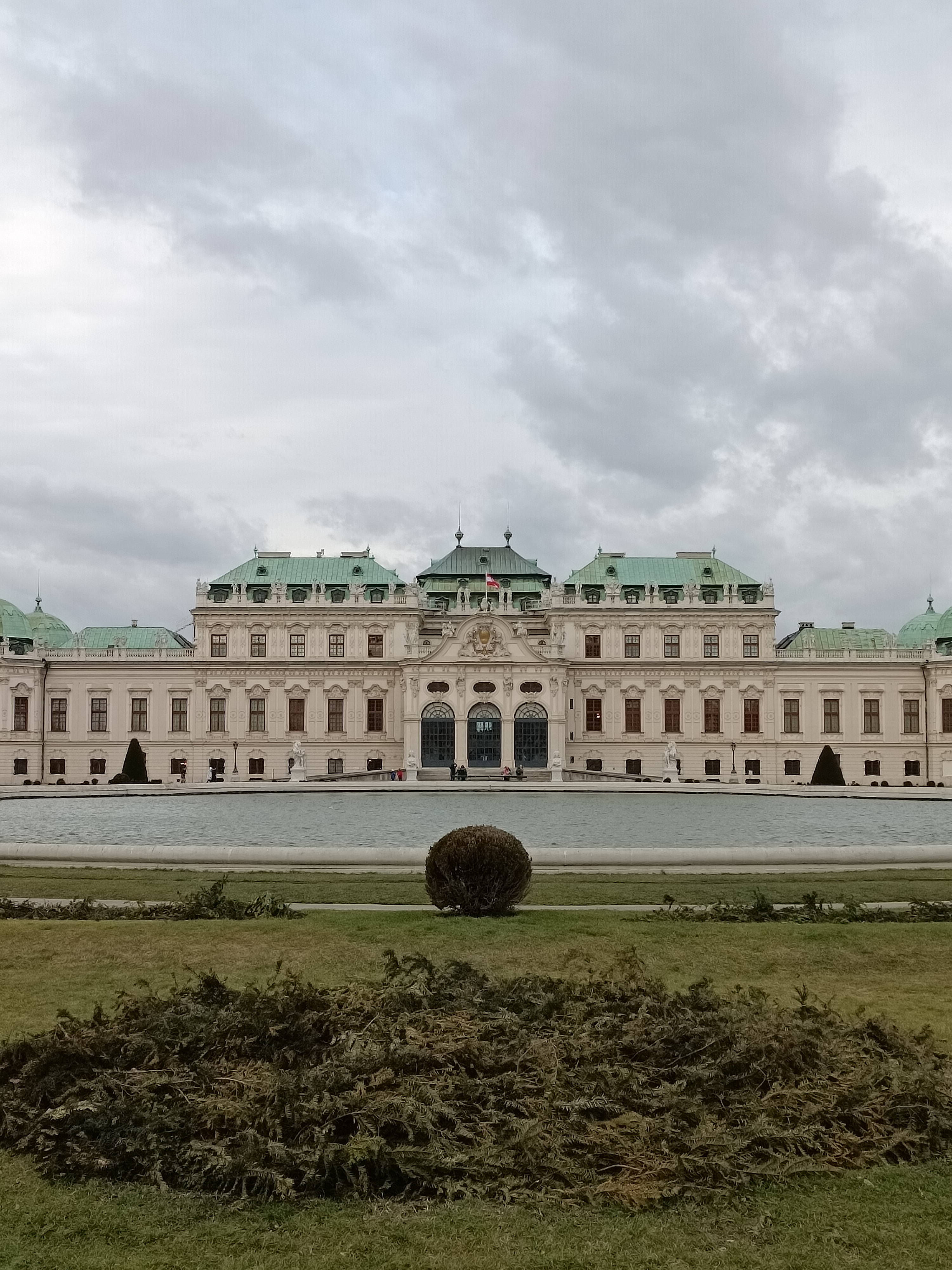Upper Belvedere Palace in Vienna featuring Baroque white architecture, green roofs, and a large reflecting pond under an overcast sky.