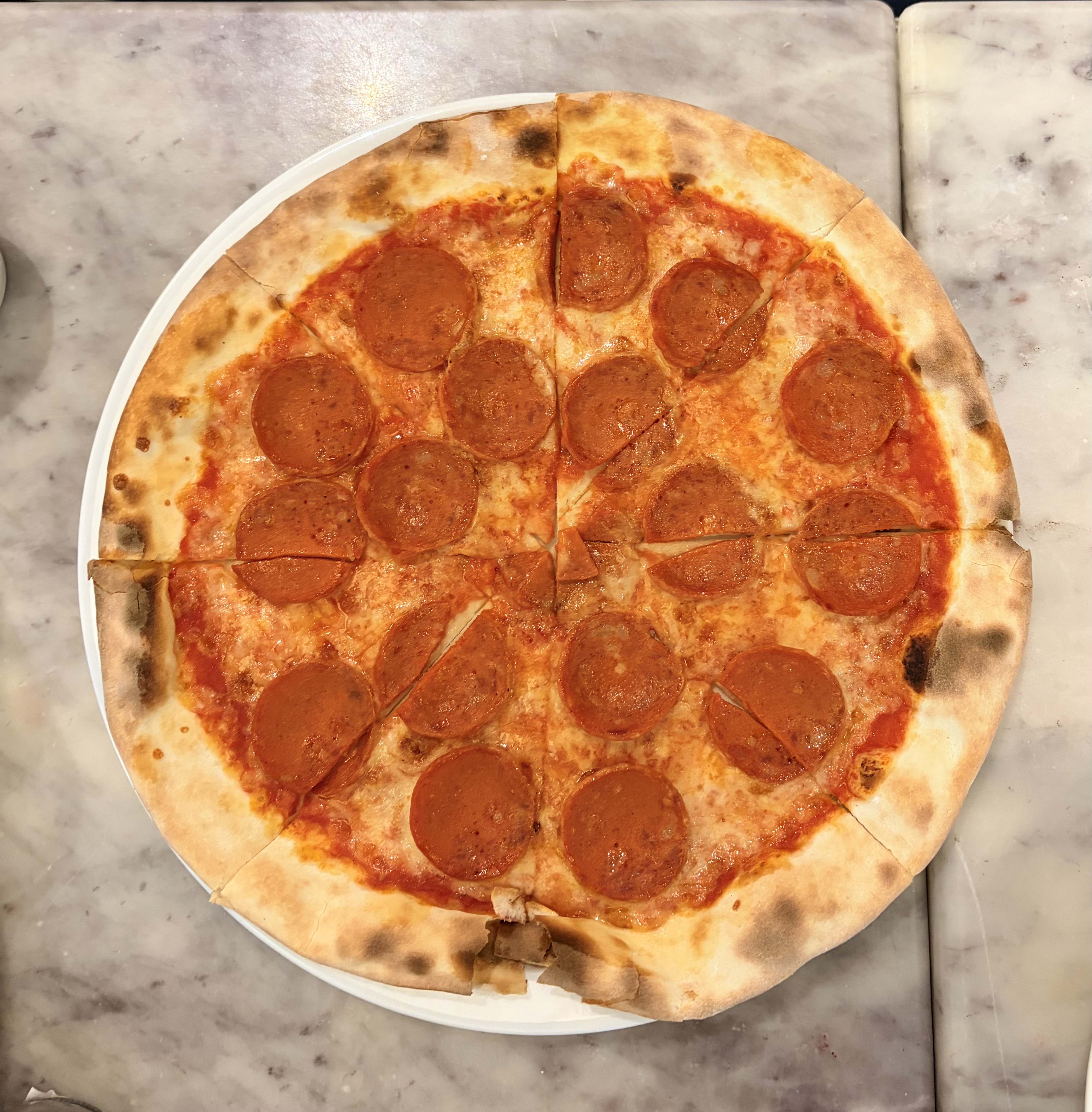 A classic wood fired pepperoni pizza with a golden, charred crust and sliced pepperoni over melted cheese and tomato sauce.