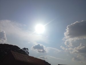 A brighter sunny day cloudy sky and dark roof and leaves on the bottom left side.