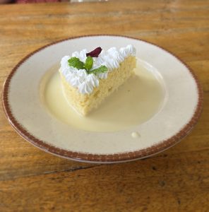 Tres leches dessert garnished with fresh mint leaves and dried rose petals, served in a white bowl.