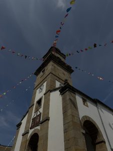 Low-angle view of a stone and white church decorated with colorful festive flags under a cloudy sky..