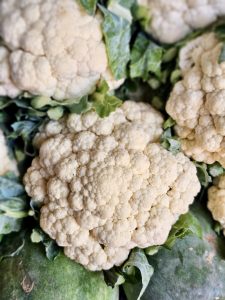 Fresh white cauliflower heads surrounded by green leaves. The detailed texture of the cauliflower florets is clearly visible, creating a strong close-up food and agriculture photograph. Location: Kuttikkattoor, Kozhikode, Kerala.