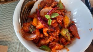 Plate of spicy chicken stir-fry with onions, bell peppers, dried red chilies, and fresh mint leaves, served on a white plate.